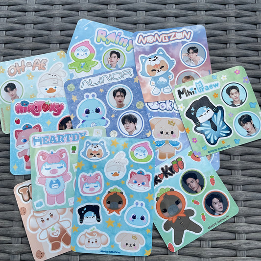 Multiple colorful cartoon character sticker sheets arranged on a gray woven surface. The sheets feature cute illustrated characters and several circular photo inserts, with visible text including 'Rain', 'Nongzun', 'Minha faew', and 'Heartty'.